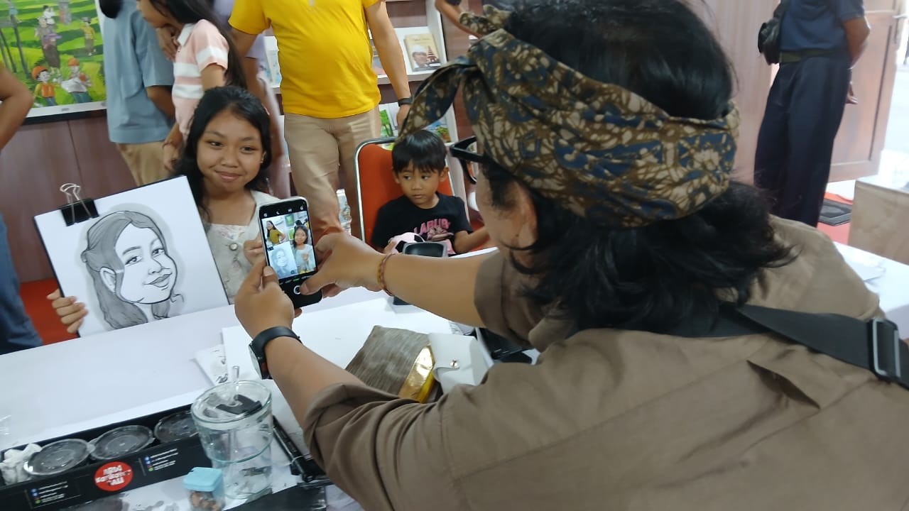 Dokumentasi. Usai mensketsa, Man Ata mendokumentasikan hasilnya bersama si pemilik wajah. Meski semakin terdesak dengan adanya teknologi AI, para kartunis Bali tak patah semangat memperkenalkan kartun ke anak-anak.