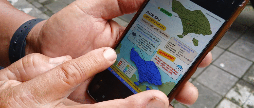 Pekaseh Subak Padanggalak, Kota Denpasar, Ketut Losen memperlihatkan whatsapp grup subaknya dari telepon genggam pintarnya mengenai informasi prakiraan cuaca dari BMKG Wilayah Denpasar, Jumat (13/2/2026). Informasi ini merupakan prakiraan cuaca setiap 10 harian (dasarian) dan membantunya beserta anggota subak mengambil keputusan untuk mengelola sawahnya kedepan. (Foto : KanalBali.id/Ayu Sulistyowati)